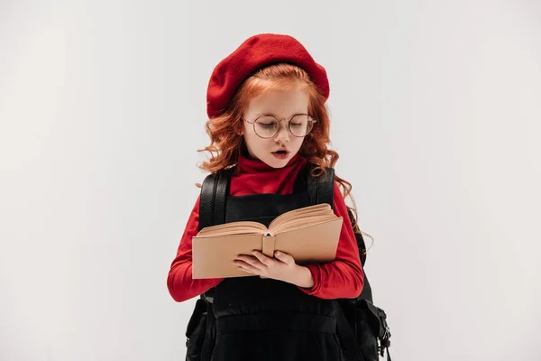 Pequeña colegiala enfocada lectura libro aislado en gris - foto de stock