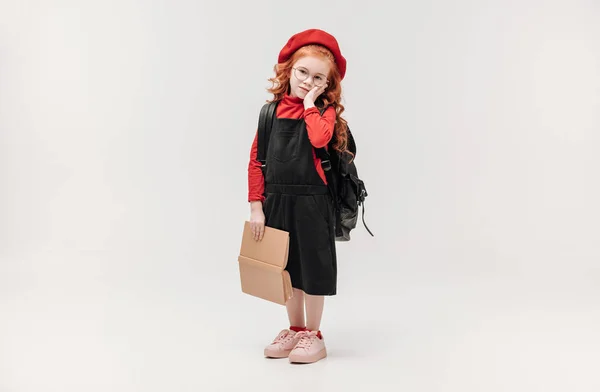 Adorable little schoolgirl with backpack and big book isolated on grey — Stock Photo