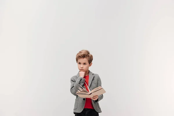 Pequeno estudante pensativo com livro isolado em cinza — Fotografia de Stock