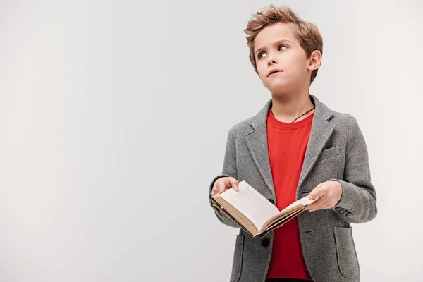 Annoiato piccolo scolaro tenendo libro isolato su grigio — Foto stock