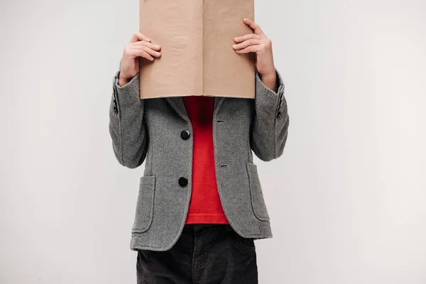 Petit écolier couvrant visage avec livre isolé sur gris — Photo de stock