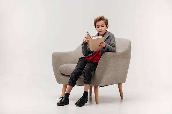 Focalizzato piccolo studente lettura libro in poltrona — Foto stock