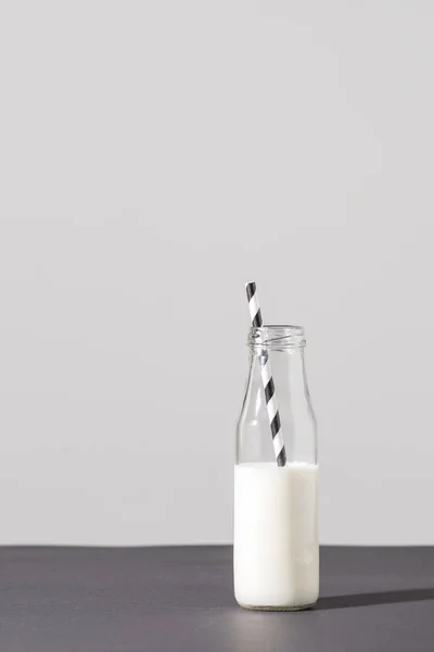 Glasflasche mit Milch und gestreiftem Trinkhalm auf grau — Stockfoto