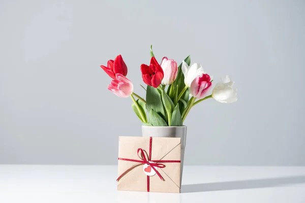 Lindas flores de tulipa florescendo em vaso e envelope em cinza — Fotografia de Stock