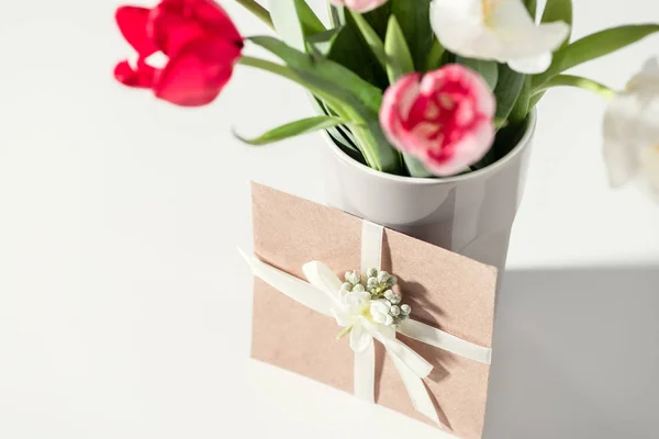 Селективный фокус красивых цветущих цветов тюльпана в вазе и конверте на сером — стоковое фото