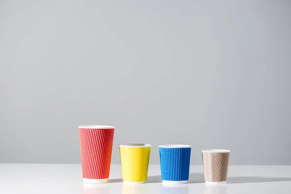 Différentes tasses en papier de couleur dans une rangée sur gris — Photo de stock