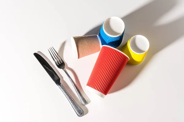 Vue de dessus des gobelets et couverts en papier coloré sur blanc — Photo de stock