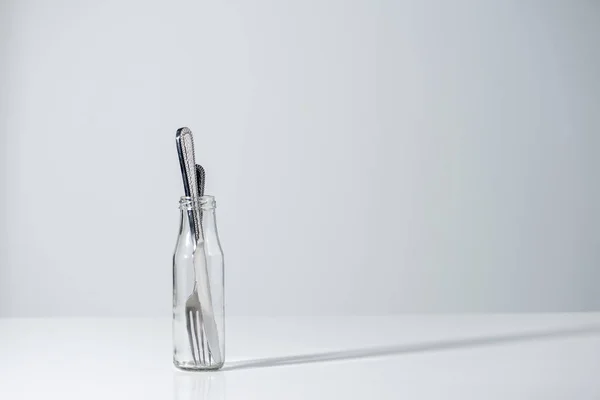 Tenedor y cuchillo en botella de vidrio con sombra sobre gris - foto de stock