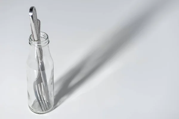 Vista ravvicinata di forchetta e coltello in bottiglia di vetro con ombra su grigio — Foto stock