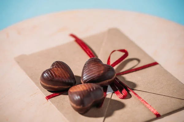 Крупный план шоколадных конфет в форме сердца на конверте с красной лентой, избирательный фокус с копировальным пространством — стоковое фото