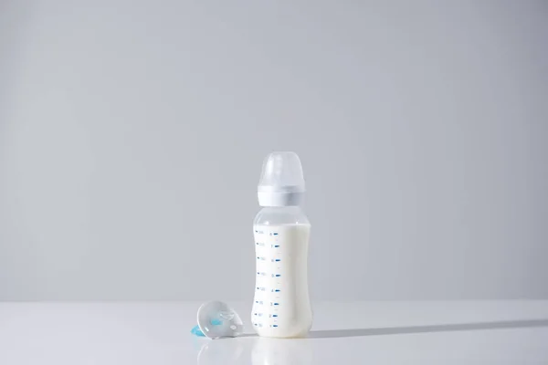 Пластиковая бутылка с молоком и соском на сером — стоковое фото