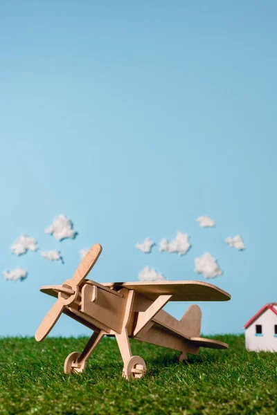 Wooden toy plane on green grass and blue sky with clouds — Stock Photo