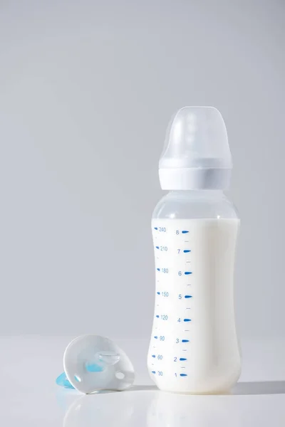 Крупный план пластиковой бутылки с молоком и соском на сером — стоковое фото