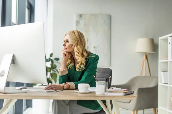 Nachdenkliche Geschäftsfrau schaut weg, während sie Desktop-Computer am Arbeitsplatz benutzt — Stockfoto