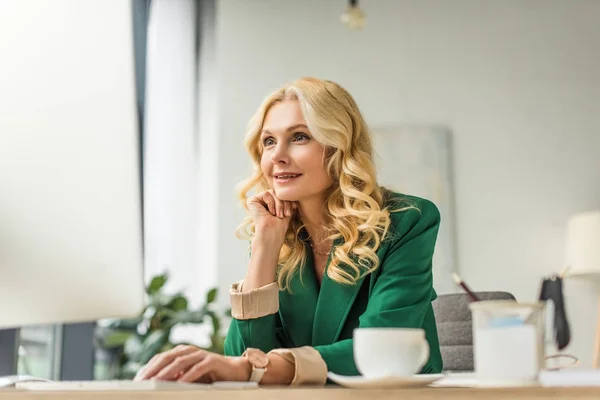 Sonriente mujer de negocios de mediana edad utilizando la computadora de escritorio en el lugar de trabajo - foto de stock