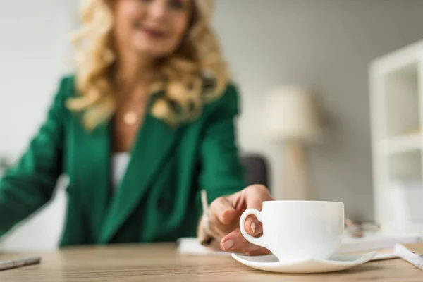 Close-up partial view of businesswoman holding cup of coffee at workplace — Stock Photo