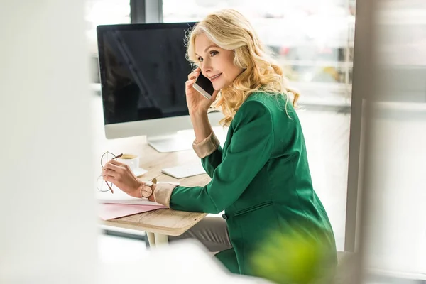 Selective focus of beautiful businesswoman talking by smartphone at workplace — Stock Photo