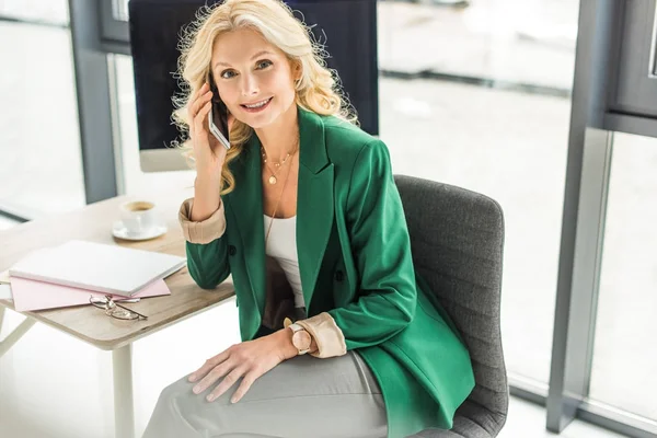 Belle femme d'affaires d'âge moyen parlant sur smartphone et souriant à la caméra — Photo de stock