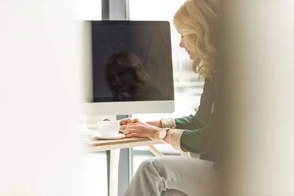 Foco seletivo da mulher de negócios que bebe café e usa computador desktop no local de trabalho — Fotografia de Stock