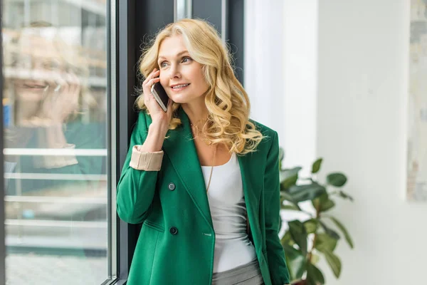 Smiling businesswoman talking by smartphone and looking at window — Stock Photo