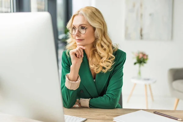 Middle aged businesswoman in eyeglasses using desktop computer at workplace — Stock Photo