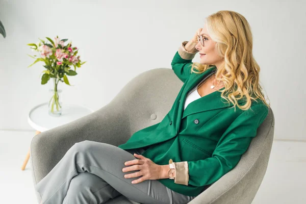 Ritratto di bella donna matura in occhiali seduta in poltrona e distogliendo lo sguardo — Foto stock