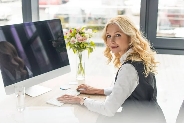 Business woman using desktop computer and looking at camera at workplace — стоковое фото