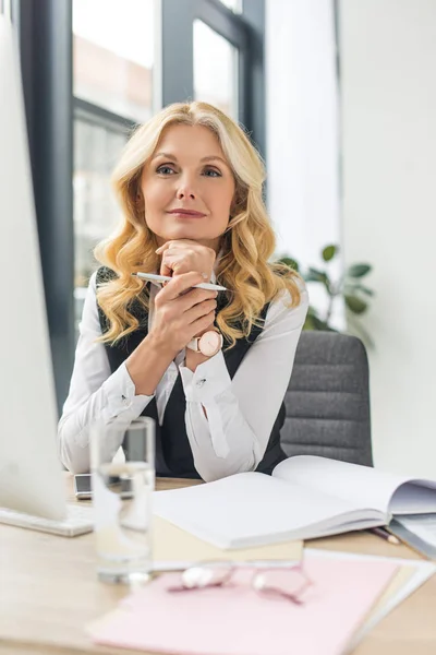 Lächelnde Geschäftsfrau mittleren Alters, die mit Papieren und Desktop-Computer arbeitet — Stockfoto