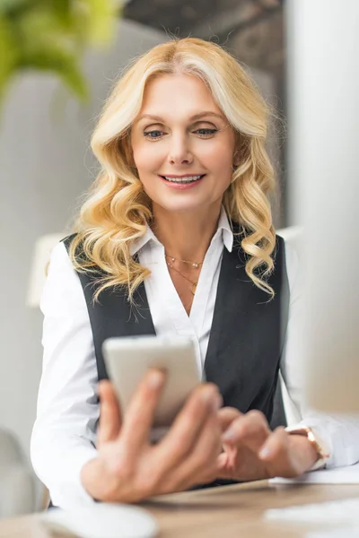 Вибірковий фокус усміхненої бізнес-леді середнього віку за допомогою смартфона — стокове фото