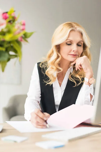 Selektiver Fokus der Geschäftsfrau mittleren Alters, die Papierkram am Arbeitsplatz erledigt — Stockfoto