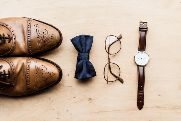 Vista superior de los zapatos, lazo arco con gafas y reloj en piso de madera - foto de stock
