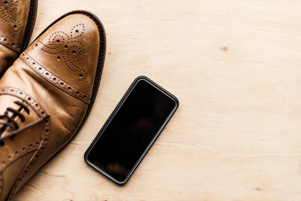 Vista superior de los zapatos de teléfono inteligente y cuero marrón en la superficie de madera - foto de stock