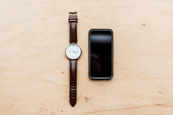 Blick von oben auf Uhr und ausgeschaltetes Smartphone auf Holztisch — Stockfoto