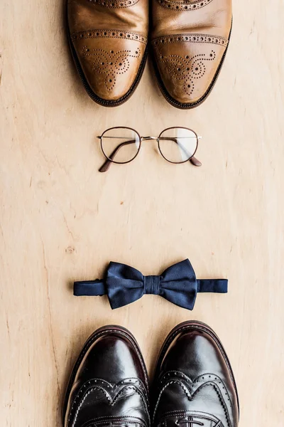 Верхний вид обуви, очков и галстука бант на деревянной поверхности — стоковое фото