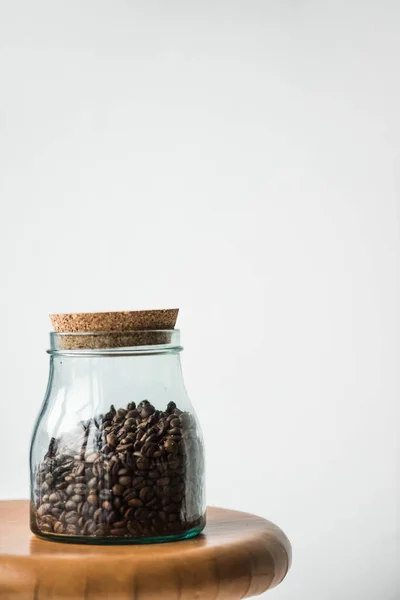 Botella de vidrio con granos de café y tapa en soporte de madera aislado en blanco - foto de stock
