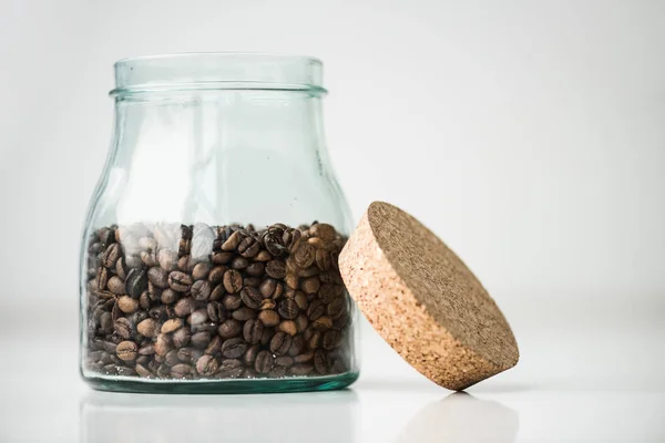 Glass bottle with coffee beans and cork on white — Stock Photo