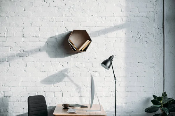 Lâmpada de mesa, computador e prateleira na parede no escritório — Fotografia de Stock