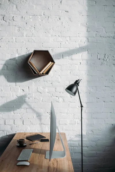 Table lamp, computer and shelf on wall in office — Stock Photo