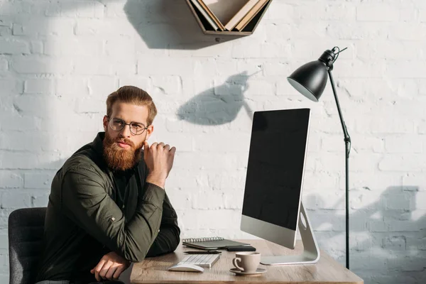 Красивый бородатый бизнесмен сидит за рабочим столом и смотрит в сторону — стоковое фото