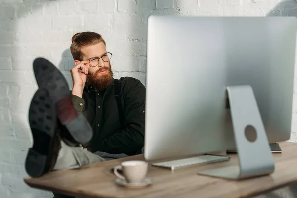 Бизнесмен сидит с ногами на офисном столе и смотрит на компьютер — стоковое фото
