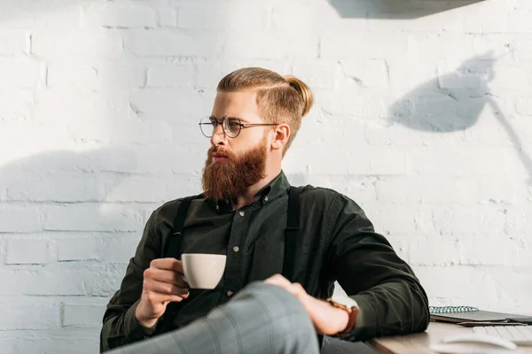 Apuesto hombre de negocios sosteniendo la taza de café y mirando hacia otro lado - foto de stock
