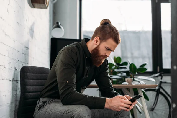 Gutaussehender Geschäftsmann sitzt und schaut aufs Smartphone — Stockfoto