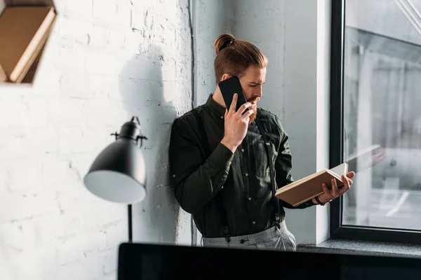 Side view of businessman talking by smartphone and looking at book — Stock Photo