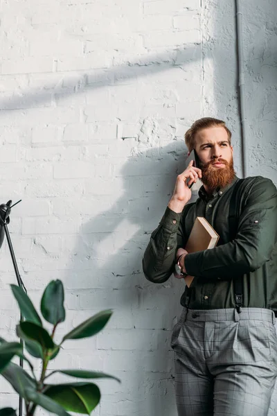 Uomo d'affari che parla con lo smartphone, tiene il libro e distoglie lo sguardo — Foto stock