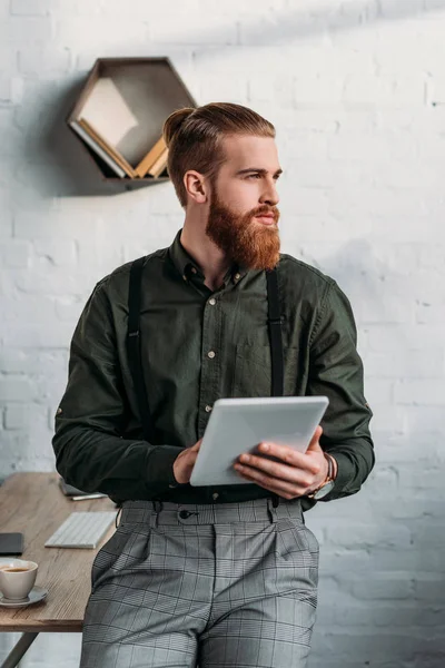Бородатый бизнесмен держит планшет и смотрит в сторону — стоковое фото