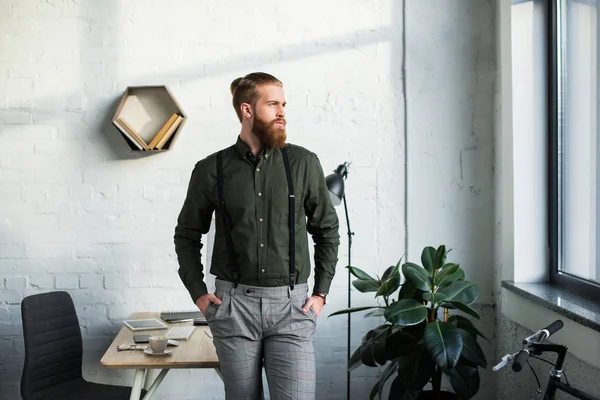Handsome bearded businessman standing in office and looking away — Stock Photo