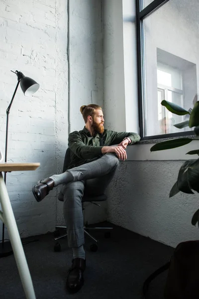 Schöner bärtiger Geschäftsmann sitzt im Büro und schaut weg — Stockfoto