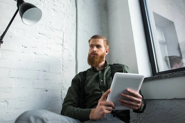 Бородатий бізнесмен тримає планшет і дивиться геть — стокове фото