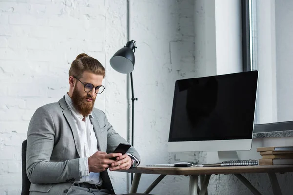 Красивый бородатый бизнесмен смотрит на смартфон в офисе — стоковое фото