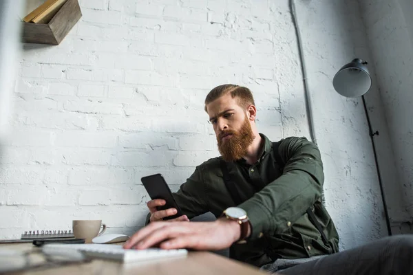 Schöner bärtiger Geschäftsmann schaut im Büro auf sein Smartphone — Stockfoto